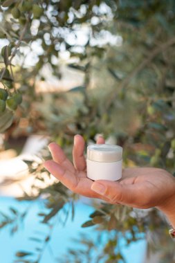 Cilt kremi modeli, beyaz tüp kadın ellerinde zeytin ağacı arka planı, cilt güvenliği