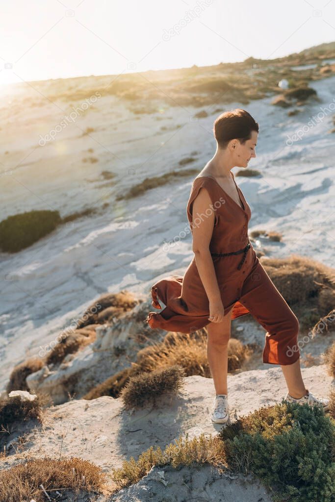 a woman in her forties with a short haircut stands in the sun at sunset and the wind blows