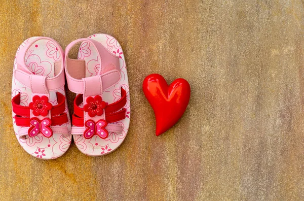 Bebek sandaleti ayakkabısı ve tahta arka planda fotokopi alanı olan bir kalp.