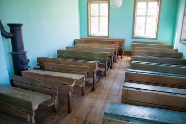 Boş tahta masaları ve bankları olan antika bir sınıf.