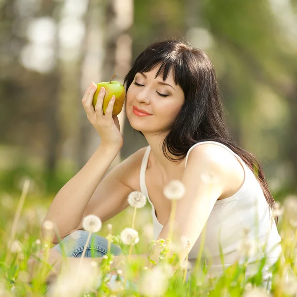 Niedliche Frau isst den Apfel im Park mit Löwenzahn — Stockfoto