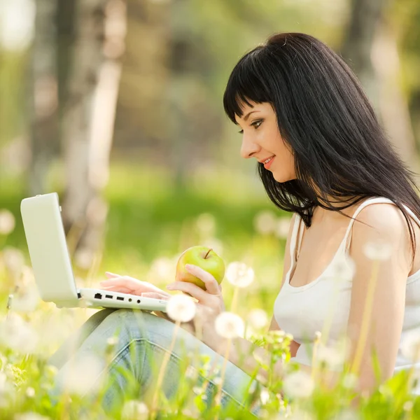 Ładny kobieta z białym laptopa w parku z mniszek lekarski — Zdjęcie stockowe