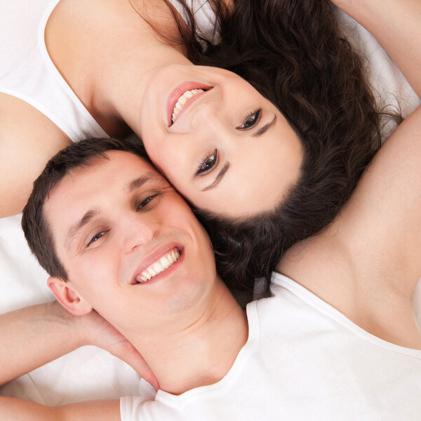 Молодая счастливая пара лежит в белой постели
