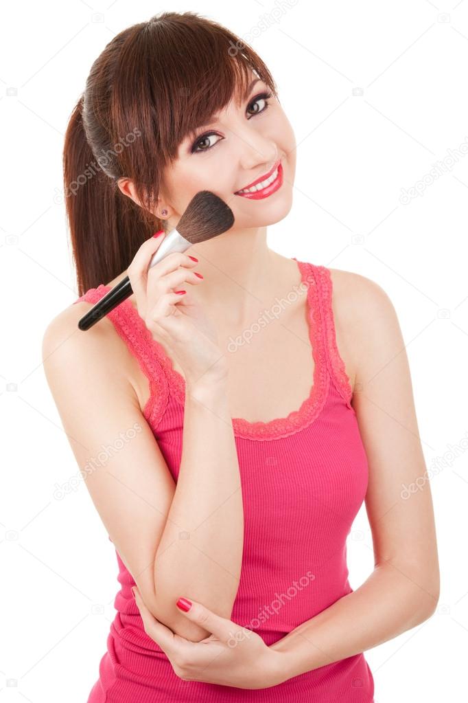 Young woman applying brush for makeup to her face, isolated on w