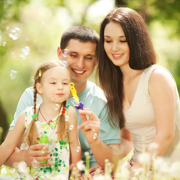 Feliz madre, padre e hija soplando burbujas en el parque — Foto de Stock