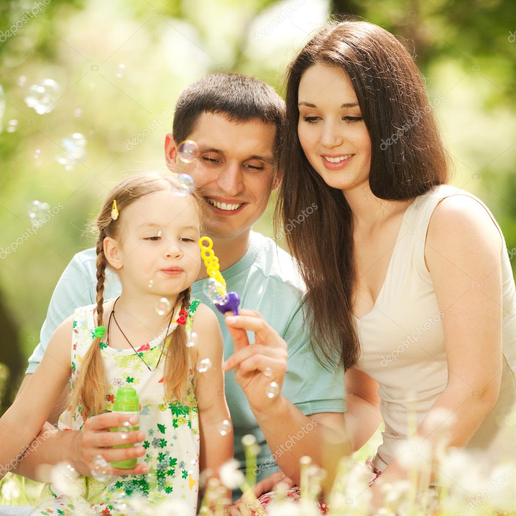Happy mother, father and daughter blowing bubbles in the park.
