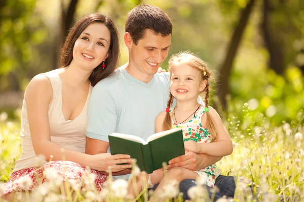 幸福的母亲、 父亲和女儿读一本书在公园 — 图库照片