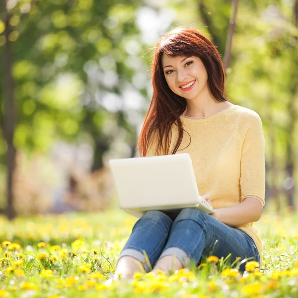 Carino donna con computer portatile bianco nel parco con denti di leone — Foto Stock