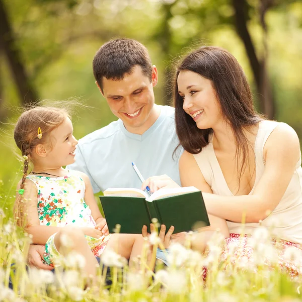 Mutlu anne, baba ve kız parkta bir kitap okumak — Stok fotoğraf