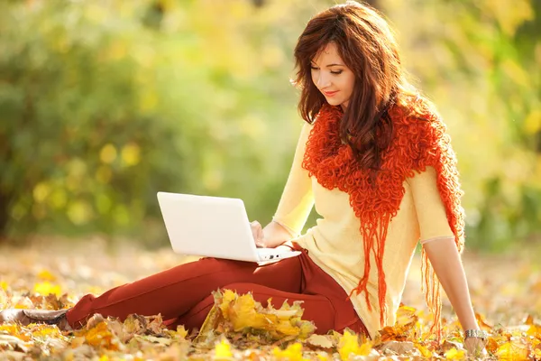 Mujer linda con portátil blanco en el parque de otoño — Foto de Stock