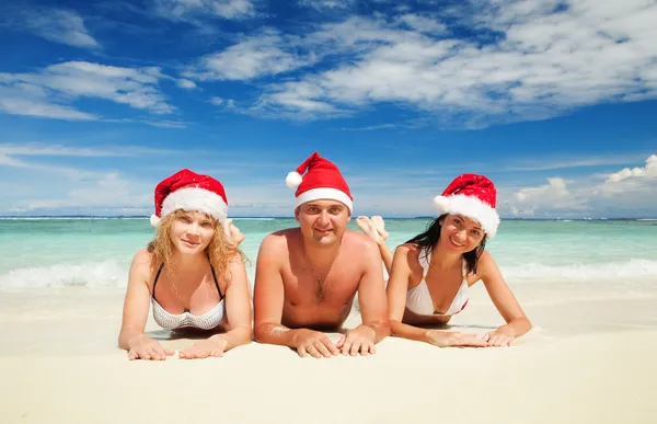 Glückliche Freunde in Weihnachtsmützen am Strand. Weihnachtsurlaub — Stockfoto