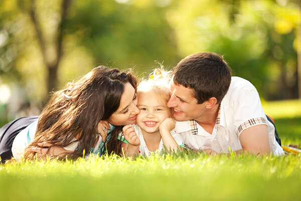 Счастливые мать и отец целуют свою дочь в парке
