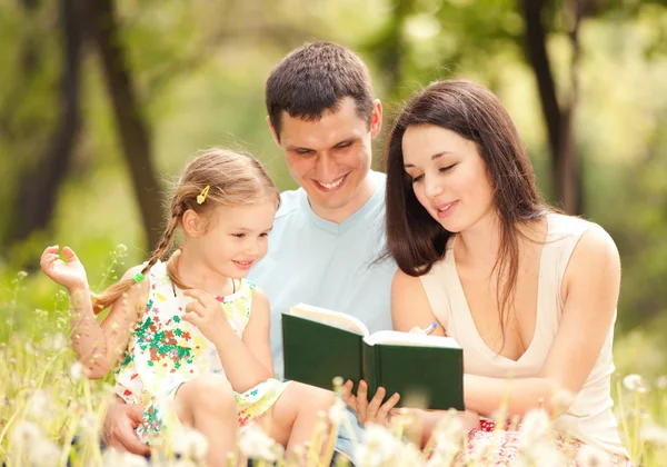 Mutlu anne, baba ve kız parkta bir kitap okumak — Stok fotoğraf