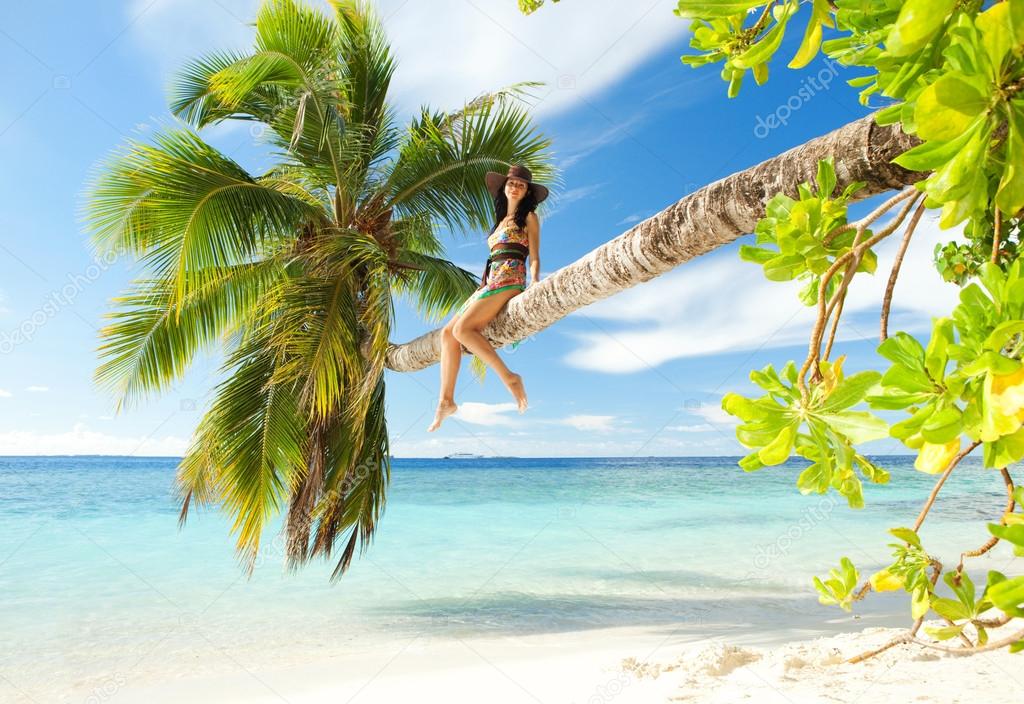 Fashion woman siting upon palm tree on the beach