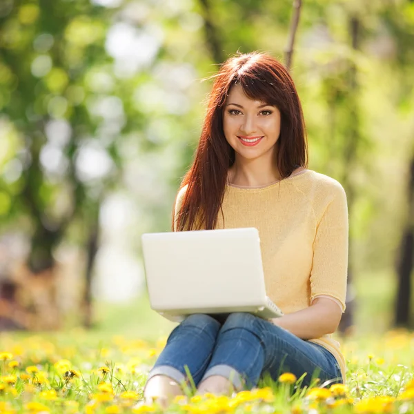 Niedliche Frau mit weißem Laptop im Park mit Löwenzahn — Stockfoto