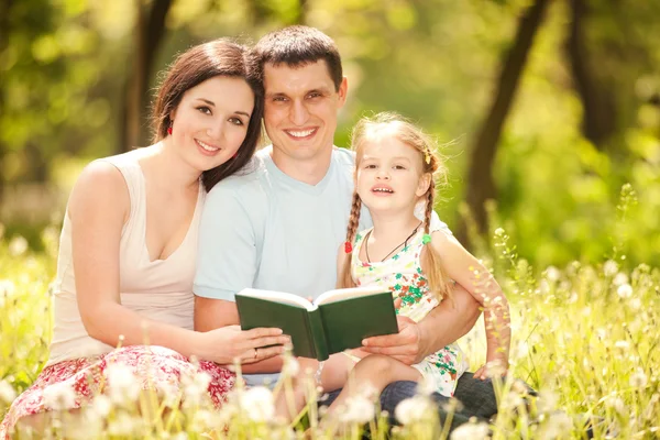 Glückliche Mutter, Vater und Tochter lesen im Park ein Buch — Stockfoto