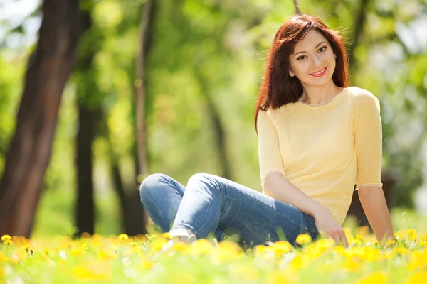 Gelukkig jongedame in het park met bloemen — Stockfoto