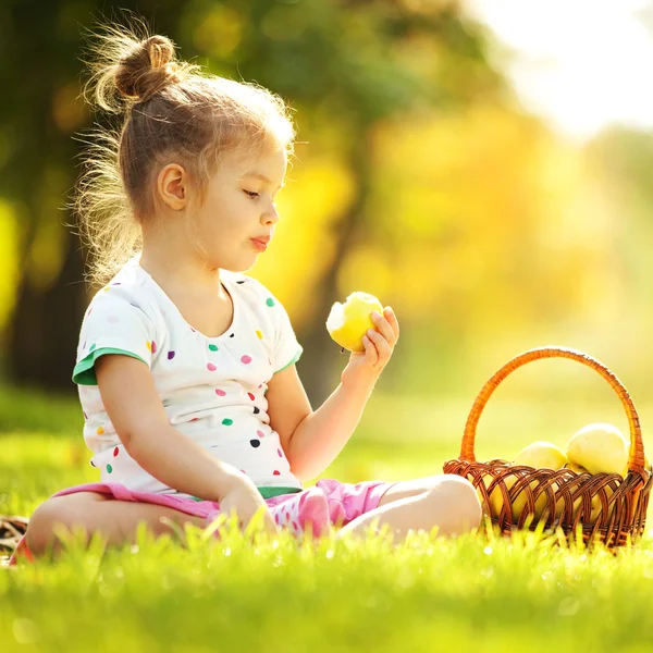 Cute little girl eating apple in the park — Stock Photo, Image