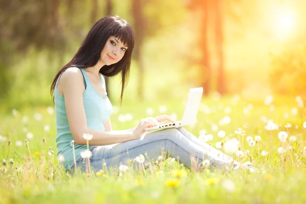 Niedliche Frau mit weißem Laptop im Park mit Löwenzahn — Stockfoto