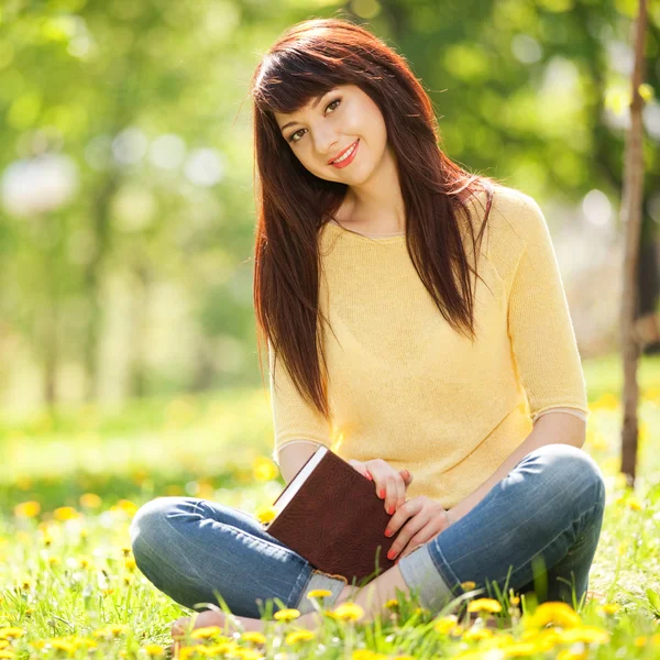 Jovem mulher lendo um livro no parque com flores — Fotografia de Stock