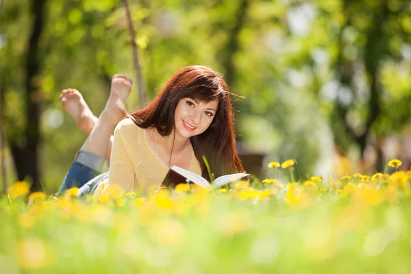 年轻女子读一书在公园与鲜花 — 图库照片