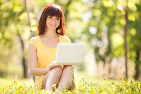 Leuke vrouw met witte laptop in het park met paardebloemen — Stockfoto