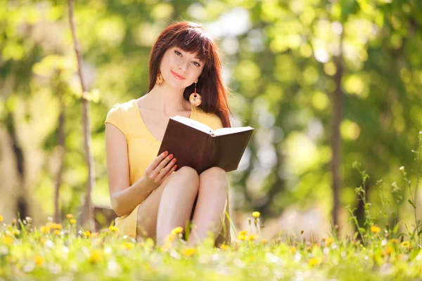 Mujer joven leyendo un libro en el parque con flores — Foto de Stock