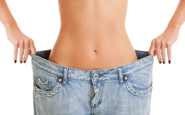 Woman shows her weight loss by wearing an old jeans, isolated on — Stock Photo, Image