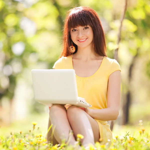 Niedliche Frau mit weißem Laptop im Park mit Löwenzahn — Stockfoto