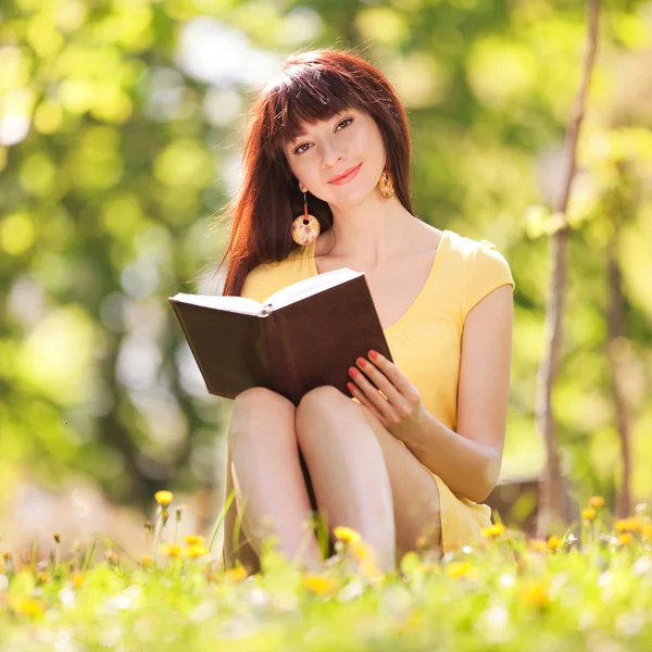 Mujer joven leyendo un libro en el parque con flores —  Fotos de Stock