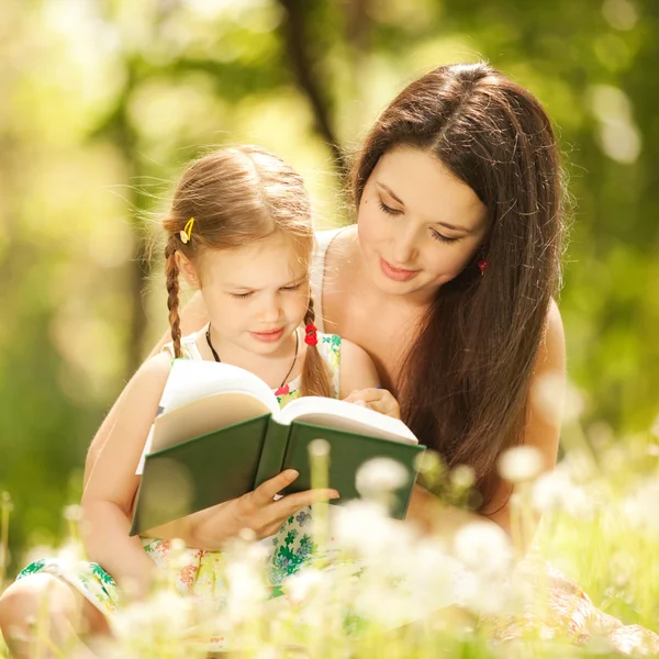 Mamma med dotter läsa en bok i parken Stockbild