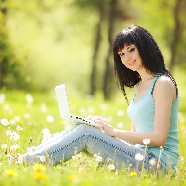 Carino donna con computer portatile bianco nel parco con denti di leone — Foto Stock