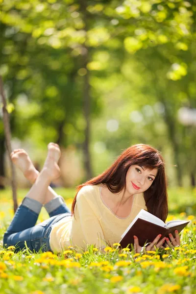 Jovem mulher lendo um livro no parque com flores — Fotografia de Stock