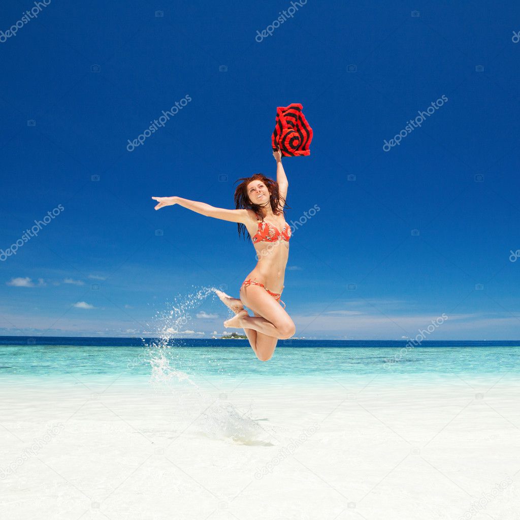 Happy young woman jumping on the beach