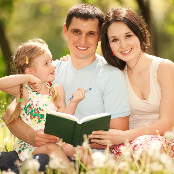 Mãe feliz, pai e filha lêem um livro no parque — Fotografia de Stock