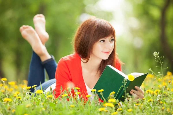 Mujer joven leyendo un libro en el parque con flores — Foto de Stock