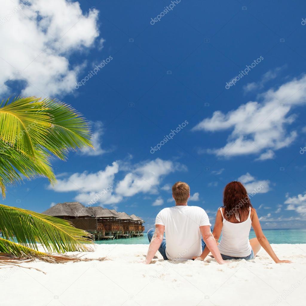 Happy couple sitting on the sunny beach