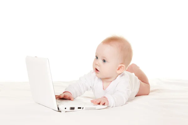 Leuke baby met laptop op het witte bed — Stockfoto