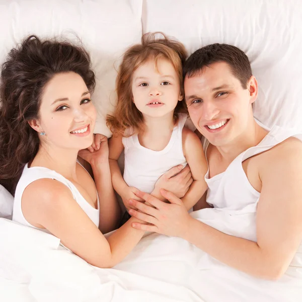 Happy family, mother, father and daughter resting on the bed — Stok fotoğraf