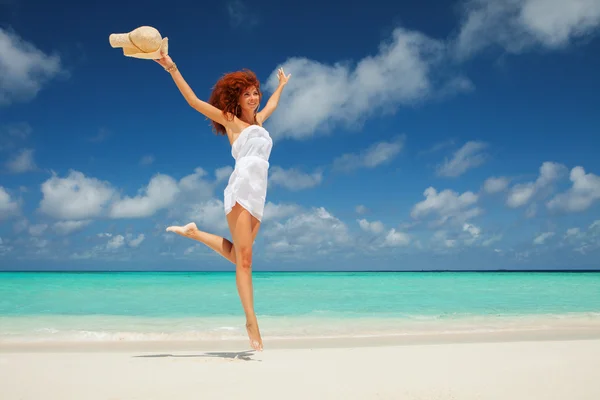Happy young woman in white dress with hat jumping on the beach — Stock Photo, Image