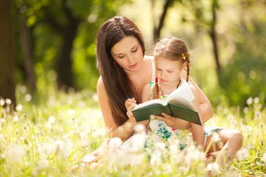 Mother with daughter read the book in the park clipart