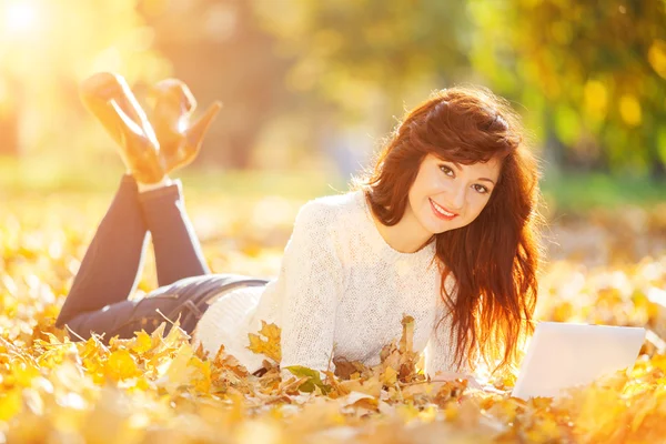 Mujer linda con portátil blanco en el parque de otoño — Foto de Stock