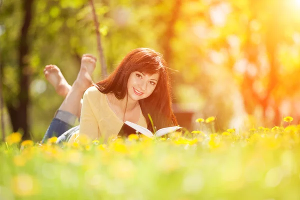 年轻女子读一书在公园与鲜花 — 图库照片