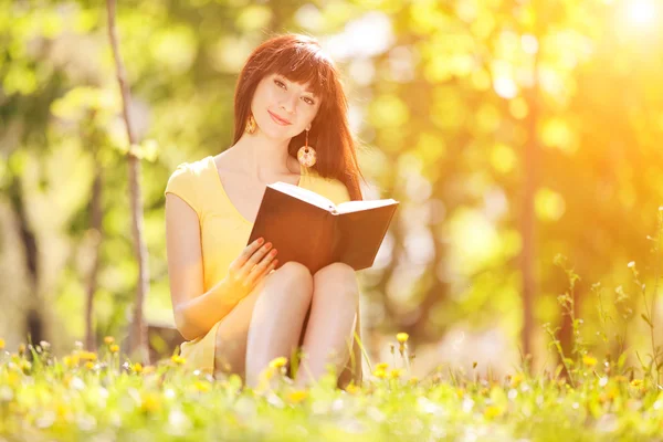 Młoda kobieta, czytanie książki w parku z kwiatami — Zdjęcie stockowe