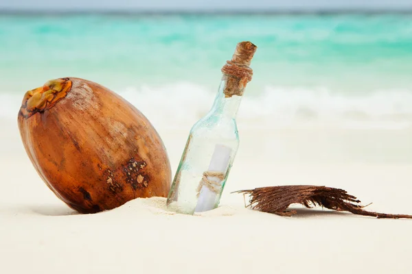 Una carta en una botella y un coco en la playa — Foto de Stock