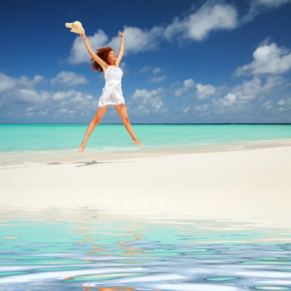 Gelukkig jonge vrouw in witte jurk met hoed springen op het strand — Stockfoto