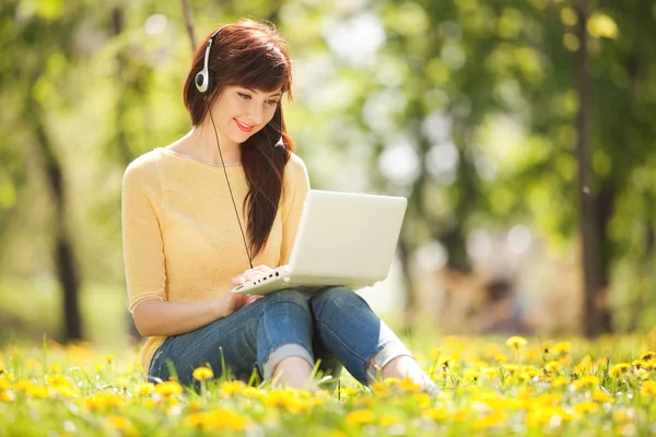 Mulher bonito em fones de ouvido com laptop branco no parque — Fotografia de Stock