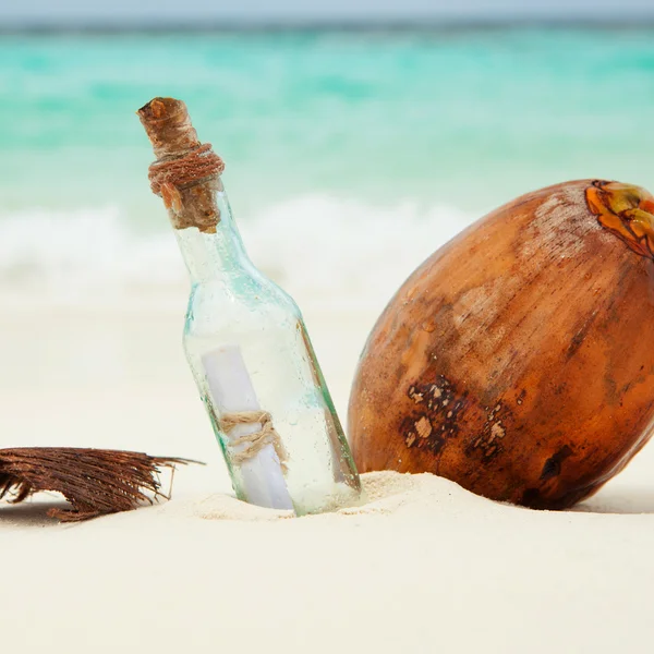 En bokstav i en flaska och en kokosnöt på stranden — Stockfoto