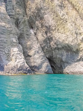 Steep Cliffs with Relief Texture Are Reflected in The Turquoise-Colored Seashore Water 