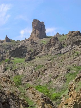 Tek başına ayakta duran ve dağların üzerine dağılmış yüksek kayalıkların arasında bir tanesi ön planda yer alıyor.